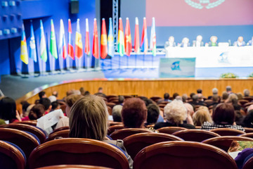 Defocused image. People in the auditorium. International conference. Flags of different countries on stage.