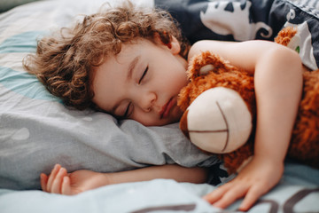 Happy boy sleeping in bed with toy bear