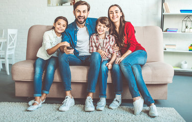 Wall Mural - Beautiful happy family watch TV on the couch at home and smiling