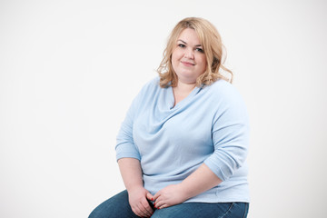 Young obese woman in casual blue clothes on a white background in the studio. Bodypositive.