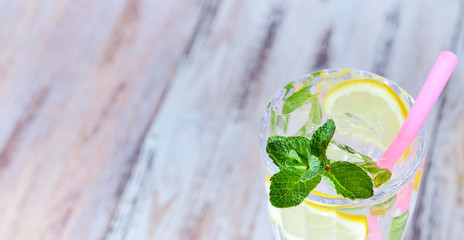 water with ice, lemon slices and mint in a glass with straw on a light wooden background. copy space. summer, refreshing drink.