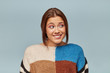 Portrait of young girl in a multi-colored sweater feels guilty anxiously looks to the side, she bit her lip, isolated on a blue background