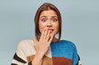 Confused young girl shrugging shoulders, having guilty look, feeling sorry for doing something wrong and making terrible mistake, keeps hand on lips, over blue background