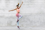 Dancer in fashion sportswear jumping over gray wall