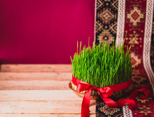 Sticker - Green fresh semeni sabzi wheat grass on vintage plate decorated with red satin ribbon against dark pink or red background on national style table cloth, Novruz spring celebration in Azerbaijan