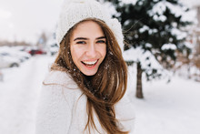Spectacular Long-haired Woman Laughing While Posing On Snow Background. Outdoor Close-up Photo Of Caucasian Female Model With Romantic Smile Chilling In Park In Winter Day.