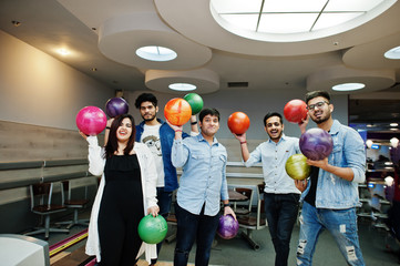 Group of five south asian peoples having rest and fun at bowling club. Holding bowling balls at hands and laughing.