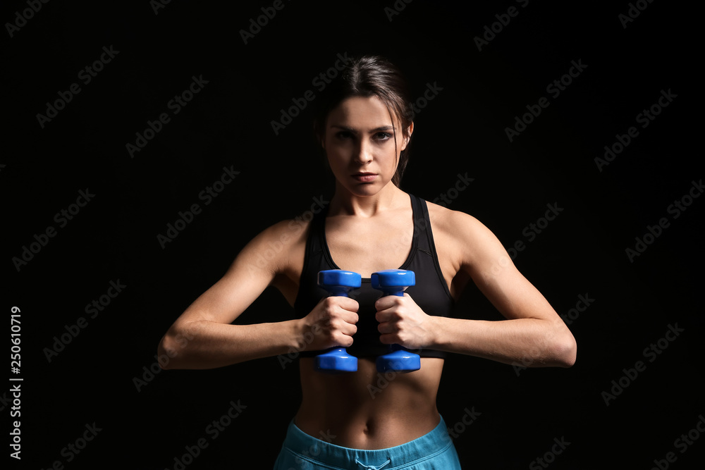 Sporty young woman with dumbbells on dark background