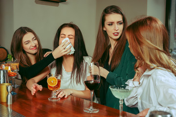 Stress. Female friends having a drinks at bar. They are sitting at a wooden table with cocktails. They are wearing casual clothes. Friends comforting and soothing a crying girl