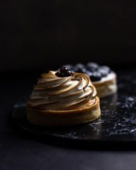 Two little tarts on the plate with cream and berries in low key style photography