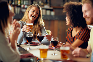 Wall Mural - Friends chatting and drinking alcohol while  sitting at restaurant. Multi ethnic group.