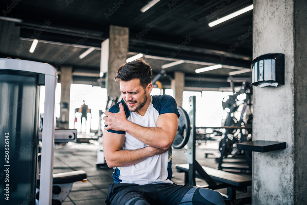 Portrait of a handsome man with strong facial expresion and injured arm while exercising in the gym. - obrazy, fototapety, plakaty 