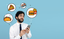 Young Man Ordering Take Away Food By Internet With A Smartphone. Fast Food Delivery App Concept. Blue Background.