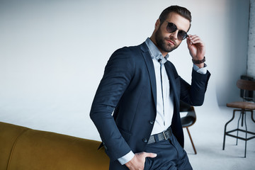 Young stylish businessman leader indoors at office wearing sunglasses looking aside thoughtful