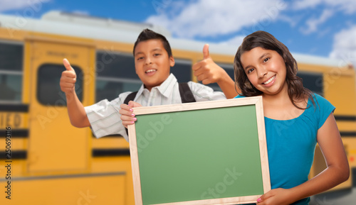 Young Hispanic Students with Blank Chalkboard Near School Bus