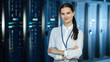 Female IT Specialist is standing at the Camera in Data Center Next to Server Racks and Looking at the Camera. Her Arms Crossed and She Smiles to the Camera.