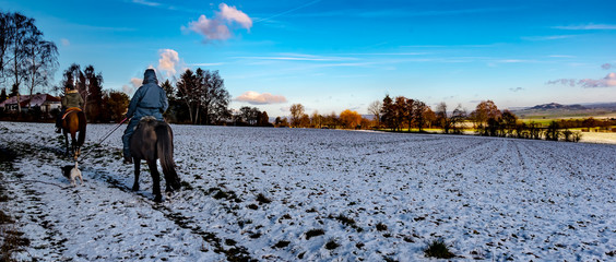 Winter Landscape, Marburg, Germany - Two riders on the horse and a dog on a leash. during a trip in winter with snow-covered fields, with a view of the Amöneburg on a sunny day.