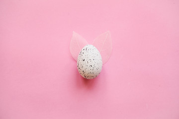 Wall Mural - Traditional easter egg on a pink background in a minimal style with leaves like Easter bunny ears.