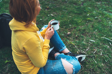 Happy girl holding in hands cup of hot tea on green grass in outdoors nature park top view, beautiful woman hipster enjoy drinking cup of coffee, lifestyle relax recreation meditation concept