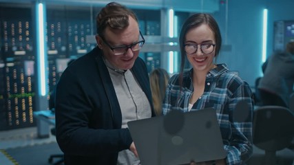 Poster - Male IT Engineer and Female IT Programmer Talking, Holding Laptop. In the Background Technical Department with Server Racks and People Working. Concept: Artificial Intelligence, Machine Learning