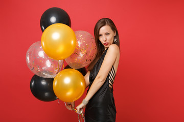 Passion young woman in little black dress celebrating, blowing lips, holding air balloons isolated on red background. International Women's Day, Happy New Year, birthday mockup holiday party concept.