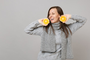 Wall Mural - Joyful young woman in gray sweater, scarf looking aside hold oranges isolated on grey background in studio. Healthy fashion lifestyle, people sincere emotions, cold season concept. Mock up copy space.