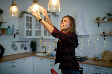 Young happy woman twists a light bulb in the kitchen lamp