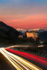 Wall Mural - light trails on road passing castle towards mountains in south tyrol - sunset/alpine glow