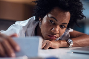 Wall Mural - Bored African American nurse photo messaging on smart phone.