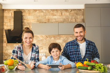 Wall Mural - Family at home standing in kitchen together looking camera happy son holding digital tablet