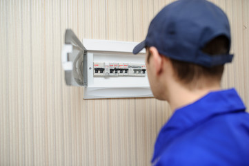 Wall Mural - lateral view of a young eletrician in blue overall disassembling a electrical panel with fuses in a house.