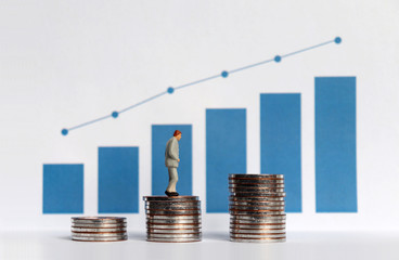 Blue bar graph with flow linear graph. The stack of coins and miniature older people. Concepts about increasing the population of the elderly and increasing the cost needed.