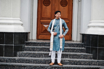 Indian man wear on traditional clothes with white scarf posed outdoor against door of building with mobile phone at  hand.