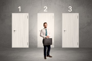 Businessman in grey room with three numbered white  door behind his back
