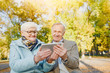 © EdNurg - Senior couple sitting on a bench in autumn park and using digital tablet