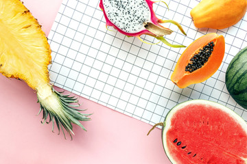 Wall Mural - Flat lay tropical summer fruit on a white grid and pastel pink background. Creative food concept with pineapple, watermelon, Hawaii papaya, dragon fruit