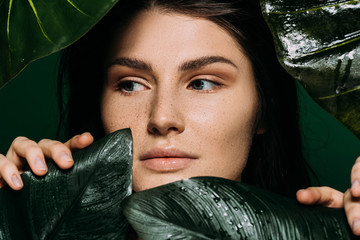 Wall Mural - attractive girl with freckles on face posing with leaves isolated on green