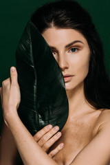 Wall Mural - beautiful young woman with freckles on face posing with leaf isolated on green