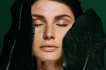 Wall Mural - portrait of beautiful girl with closed eyes posing with green leaves isolated on green