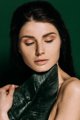 Wall Mural - portrait of beautiful woman with freckles on face posing with palm leaf isolated on green