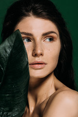 Wall Mural - portrait of beautiful girl with freckles on face posing with leaf isolated on green