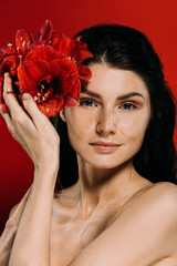 Wall Mural - beautiful woman with freckles on face posing with amaryllis flowers, isolated on red