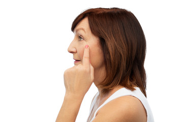 Sticker - beauty, skin aging and old people concept - profile of senior woman pointing to her eye wrinkles over white background