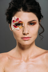 Wall Mural - beautiful brunette woman with floral petals around eye isolated on grey