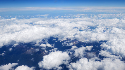 Wall Mural - Flying over fluffy white clouds with a partial view of the rural landscape far beneath. Picturesque moving cloudscape view from airplane window.