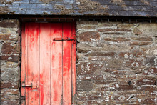Red And Distressed Wooden Door On An Old Stone Barn With Slate Tiles