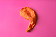 Orange deflated balloon on color background, top view