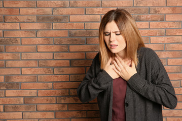 Wall Mural - Woman suffering from cough near brick wall. Space for text