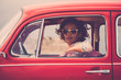 © simona - Serious lady on a old retro nice red car looking at you with open window glass - traveler with hippy freedom lifestyle and alternative vehicles