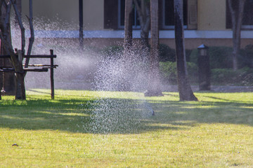 Automatic Garden Lawn sprinkler on a sunny summer day during watering the green grass field. Lawn sprinkler spaying water over green grass. Irrigation system concept.